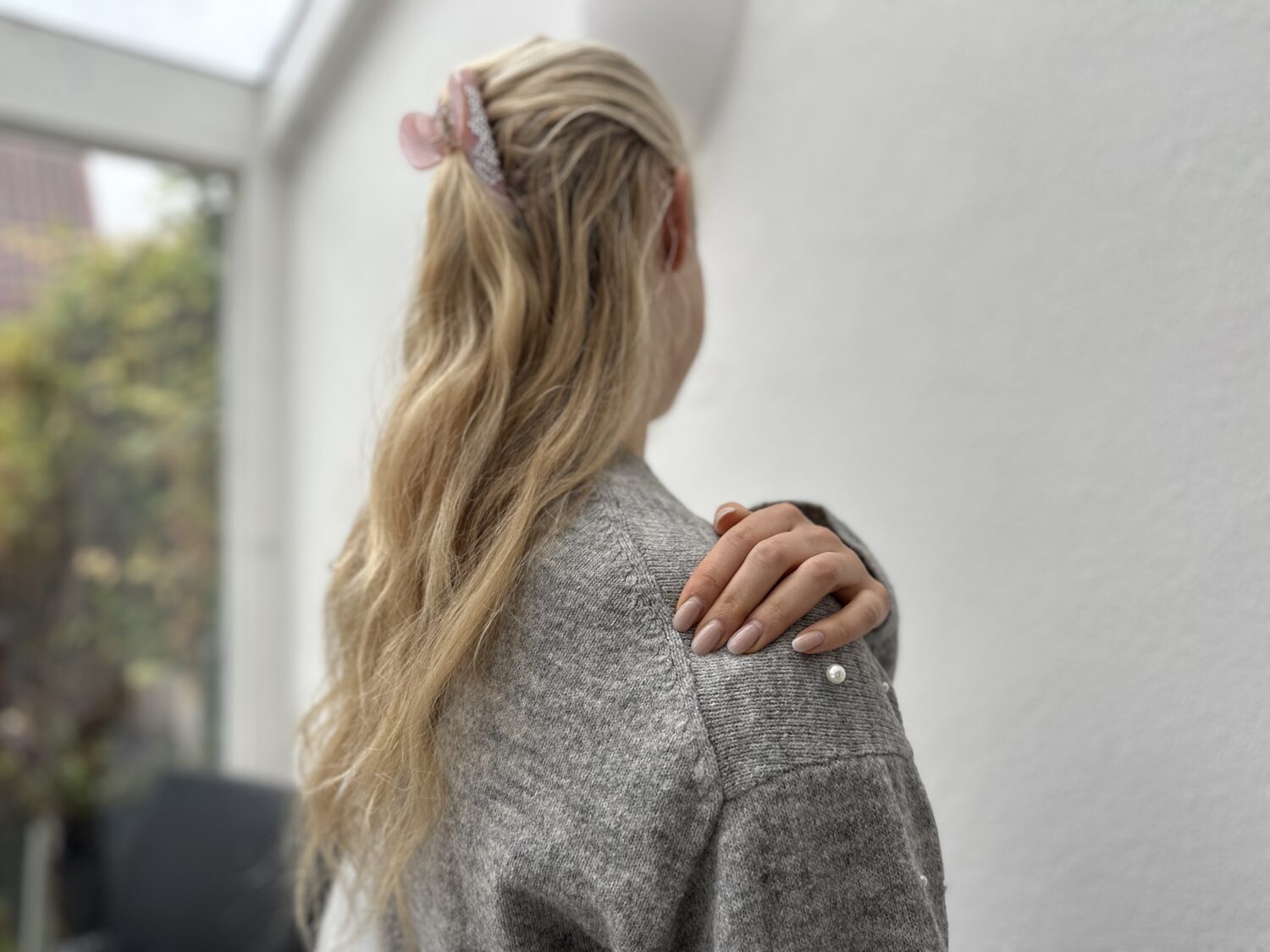 Schulterluxation: Schulter ausgekugelt | Radiologie Mühleninsel. Bild von junger Frau mit langen blonden Haaren, die sich an die rechte Schulter fasst von hinten. sie steht in einem wintergarten und hat eine graue strickjacke an Schulter ausgekugelt? Erfahren Sie, welche Symptome auf eine Schulterluxation hinweisen, und welche unsere Untersuchungen empfohlen sind.