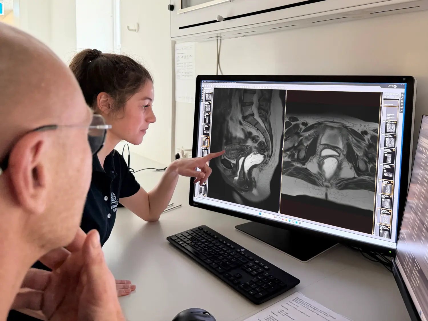 MRT-Defäkographie Radiologen besprechen Befund des MRT Bildes, eine Radiologin deutet auf das Bild, ihr Kollege, ein Radiologe mit Brill sieht zu.